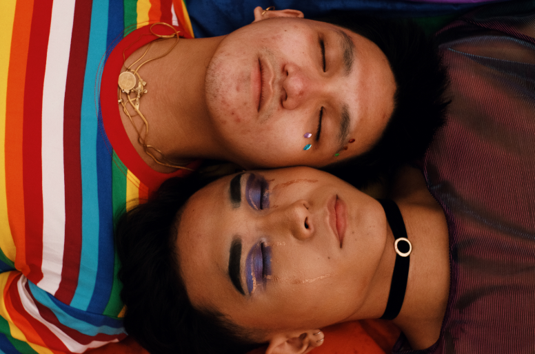 two LGBTQ+ people lying side by side, faces together.