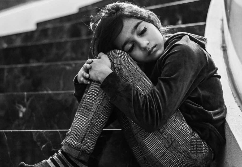 Child sitting on some steps hugging knees and looking sad