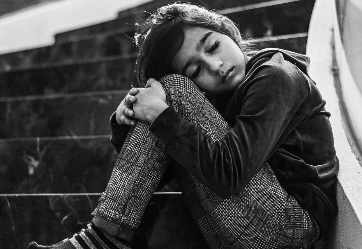 Child sitting on some steps hugging knees and looking sad