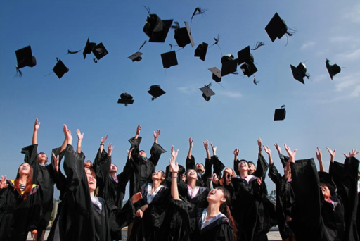 A group of graduates throwing their mortar boards (hats) into the air against a blue sky.  An image by Hippo px on Wikimedia.
