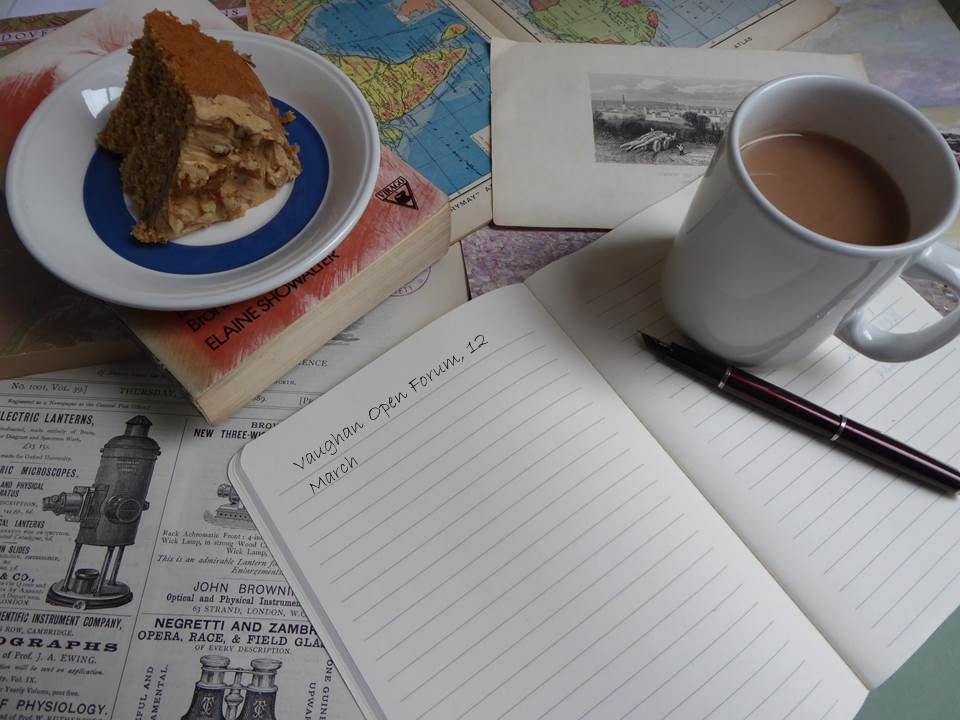 An open note book with a cup of tea and piece of cake. The notebook is lying on a layer of maps, images and texts.