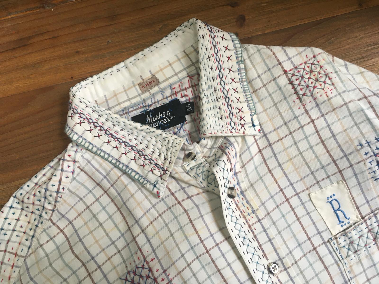 A photo of a white checked shirt with visible mending on the collar and shoulders. There is a 'R' above the shirt breast pocket.