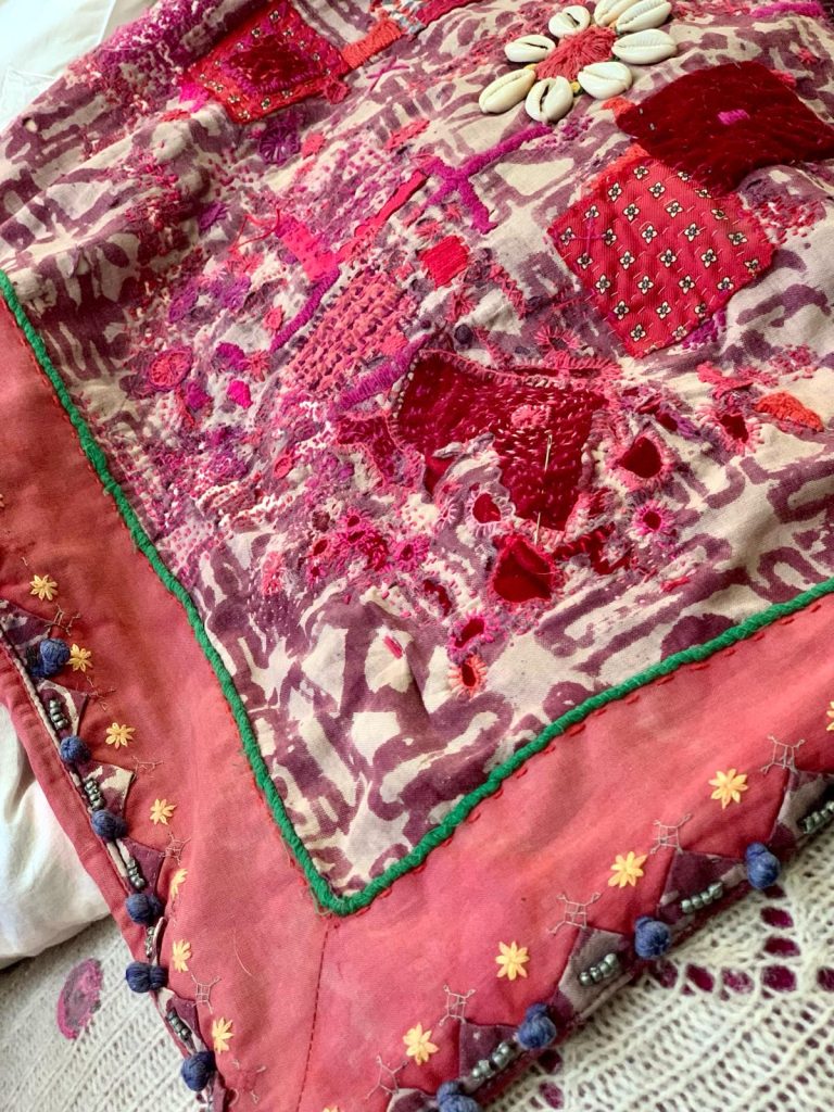 Visible repair of a red cushion cover using patches and stitching.
