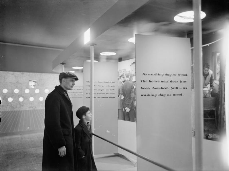 Man and boy (father and son?) look at photographs and  display panels at the 'London Pride' exhibition, held at Charing Cross underground station. The exhibition aimed to show visitors that life was going on as usual, despite the air raids and other hardships faced by Londoners.