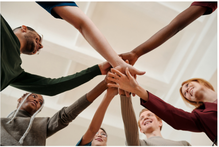 A group of people in a circle with their hands on in a stack in the middle.